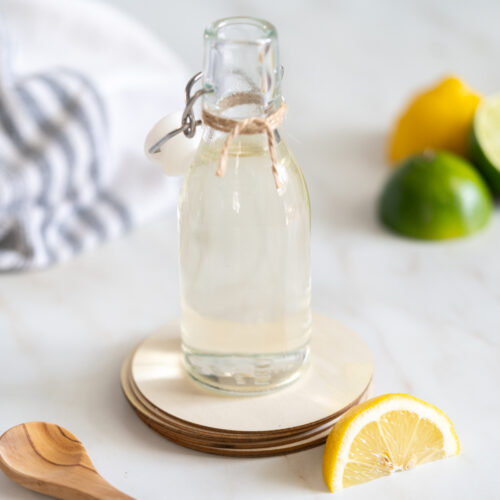 Microwave simple syrup in bottle with lemon slices and a wooden spoon.